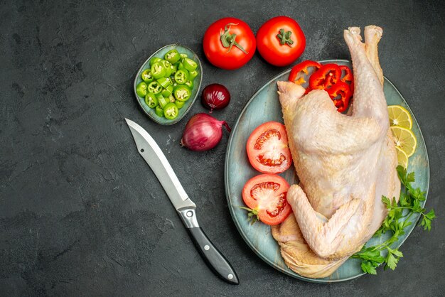 Top view raw fresh chicken inside plate with greens and vegetables on dark background