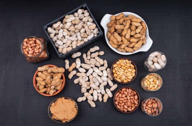 Free photo top view raw, fresh, fried peanuts and peanut butter in box, jar and bowl, on dark