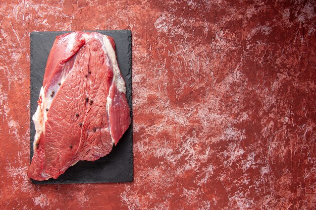 Top view of raw fresh red meat on black board on the right side on oil pastel red background with free space