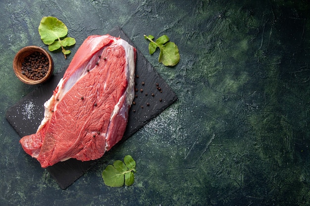 Top view of raw fresh red meat on cutting board pepper on green black mix colors background