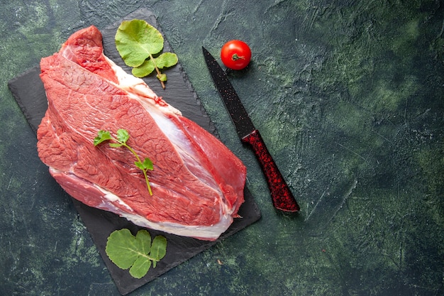 Вид сверху сырого свежего красного мяса и зелени на разделочной доске, нож, помидор на зеленом черном фоне цветов