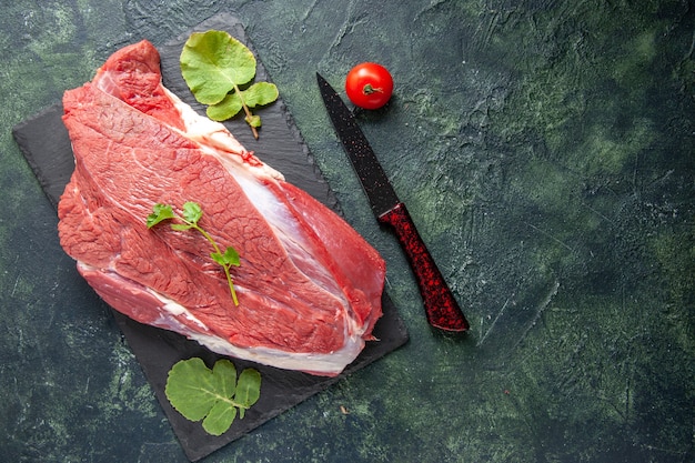 Top view of raw fresh red meat and greens on cutting board knife tomato on green black mix colors background