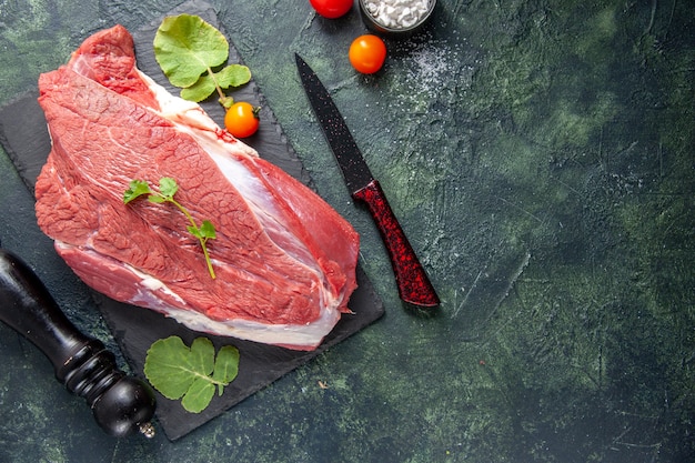 Top view of raw fresh red meat and greens on cutting board knife tomatoes wooden hammer on green black mix colors background