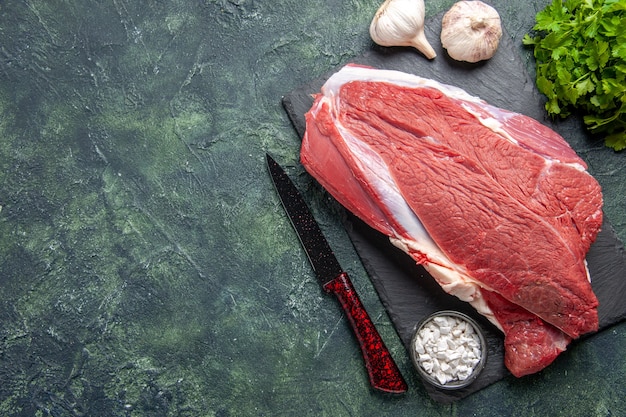 녹색 검정 혼합 색상 배경의 왼쪽에 있는 커팅 보드에 있는 원시 신선한 붉은 고기와 소금 녹색 번들 칼의 상단 보기