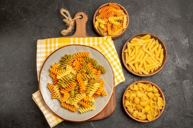 Вид сверху сырые итальянские макароны разных форм внутри тарелок на сером