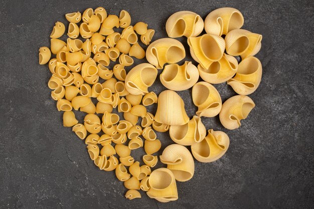 Top view of raw italian pasta forming heart shape on the dark surface