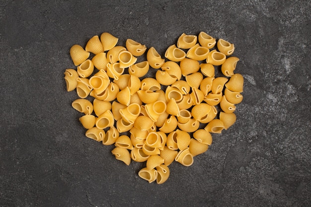 Top view of raw italian pasta forming heart shape on the dark surface