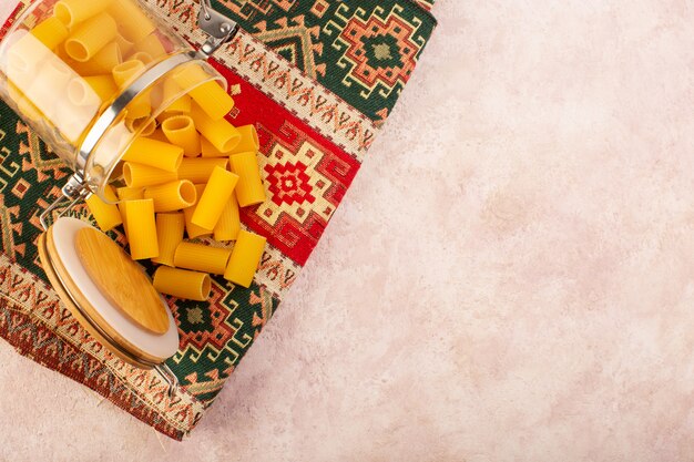 A top view raw italian pasta inside little glass kettle on colorful carpet