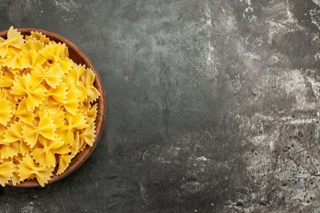 Top view raw italian pasta inside plate on dark-grey background