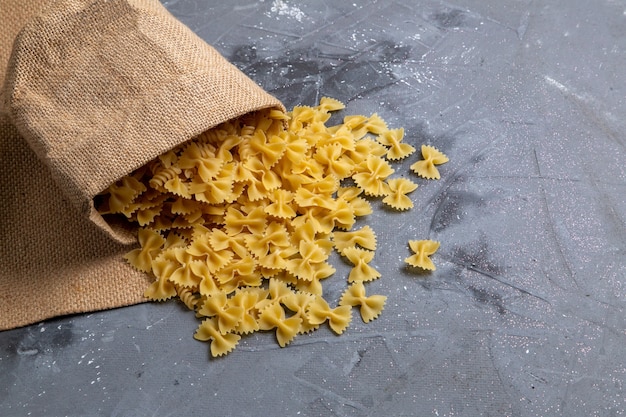 灰色の机の上のパスタのイタリア料理の食事の袋の中に少し形成された生のイタリアンパスタの平面図