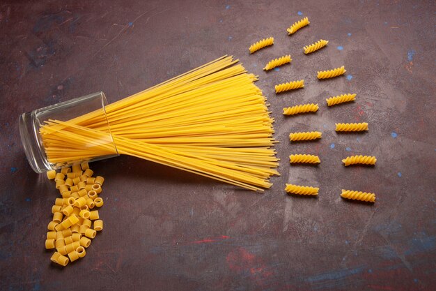 Вид сверху сырые итальянские макароны длинной формы желтого цвета на темном фоне макароны из итальянского теста пищевой краситель