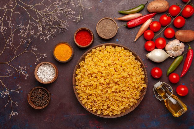 Top view raw italian pasta with different seasonings and fresh vegetables on dark background product ingredient meal food vegetable