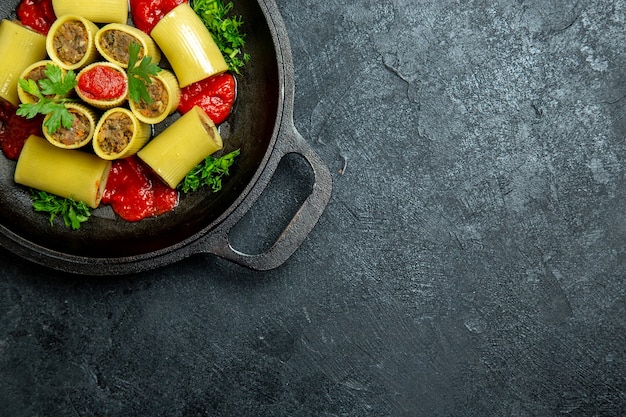 Вид сверху сырые итальянские макароны с мясной зеленью и томатным соусом внутри сковороды на темном фоне еда из теста для макаронных изделий