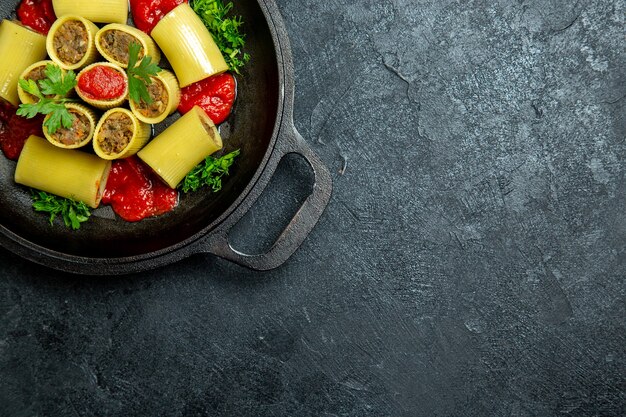 Вид сверху сырые итальянские макароны с мясной зеленью и томатным соусом внутри сковороды на темном фоне еда из теста для макаронных изделий