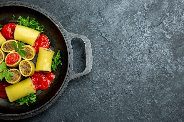 Вид сверху сырой итальянской пасты с мясной зеленью и томатным соусом внутри сковороды на темном полу из теста для макаронных изделий