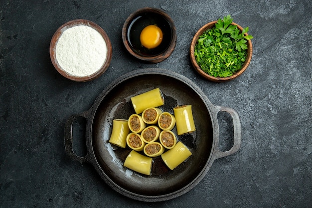 Top view raw italian pasta with meat inside pan and with greens on a dark background pasta dough meal food