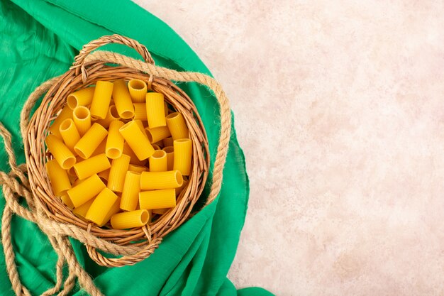 A top view raw italian pasta yellow inside little basket along with ropes on green tissue and pink