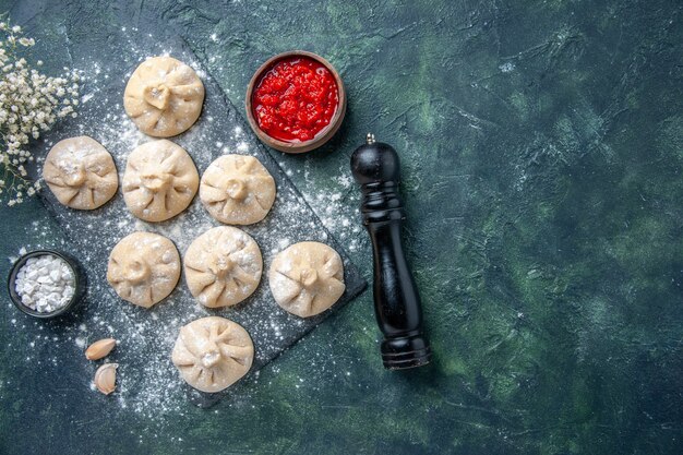 Вид сверху сырые маленькие пельмени с мясом внутри на темном фоне мука мясо перец цвета тесто приготовление еды блюдо кухни