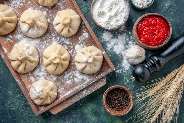 Top view raw little dumplings with meat inside on dark surface color meal dish cooking flour dough