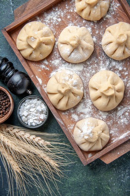 Вид сверху сырые маленькие пельмени с мясом внутри на темной поверхности цветное блюдо из муки из теста мясо