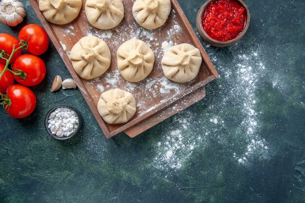 Top view raw little dumplings with meat and tomatoes on the dark background meal color flour dish dough meat cooking