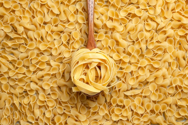 Free photo top view raw little pasta with brown wooden spoon color dough food