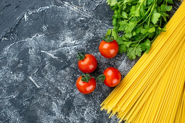 Free photo top view raw long pasta with greens and tomatoes on gray background color kitchen pasta dough food kitchen cuisine