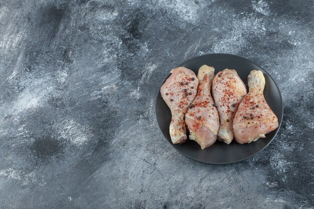 Top view of raw marinated chicken legs on black plate over grey background.