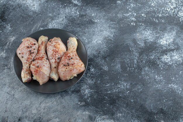 Top view of raw marinated chicken legs on black plate.