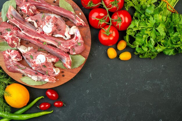 Вид сверху ломтики сырого мяса со свежими овощами и зеленью на темном фоне