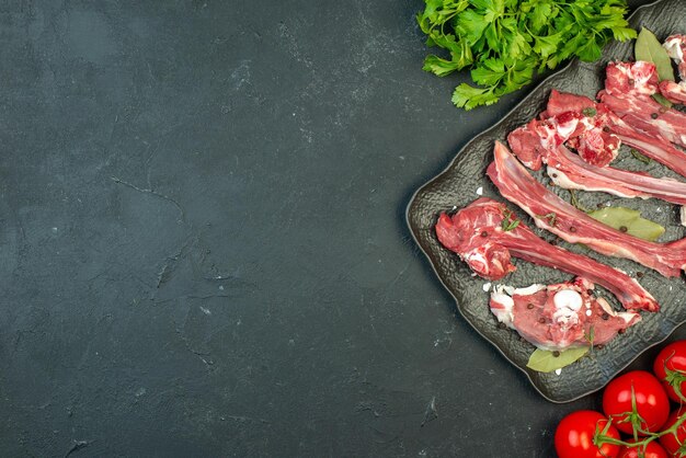 Вид сверху ломтики сырого мяса с зеленью и красными помидорами на темном фоне блюдо мясо мясник еда салат приготовление пищи
