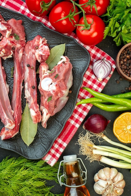 Вид сверху ломтики сырого мяса с зелеными приправами и красными помидорами на темном фоне блюдо мясо мясник ужин салат приготовление пищи Premium Фотографии
