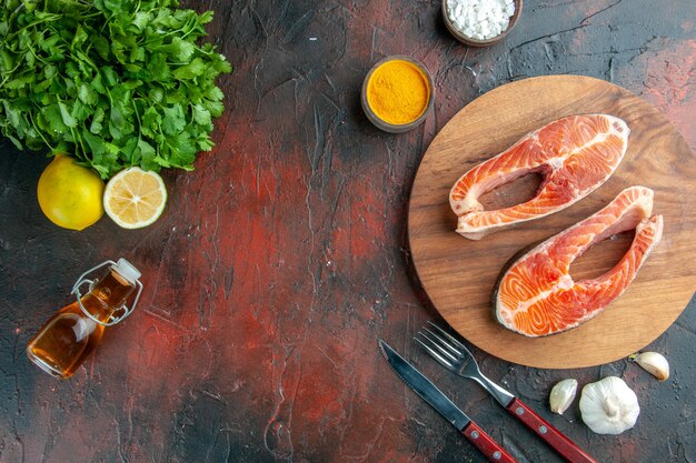 Top view raw meat slices with greens and seasonings on dark background