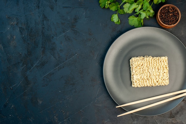 Top view raw noodles inside plate with sticks on dark-blue wall free place