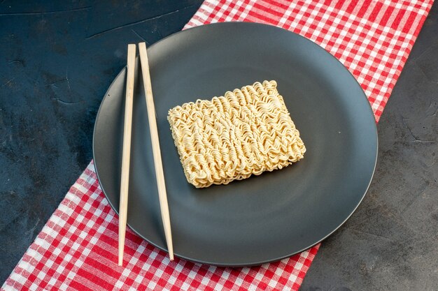 Top view raw noodles inside plate with sticks on a dark wall