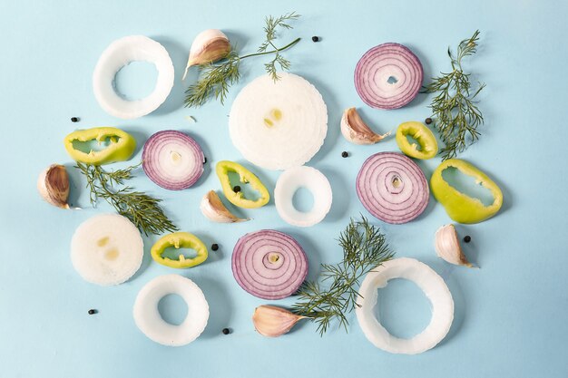 Top view of raw onion rings with yellow pepper, peppercorns, garlic and dill on a blue surface
