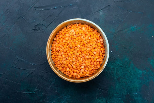 Top view of raw orange lentil inside round pot on dark blue surface