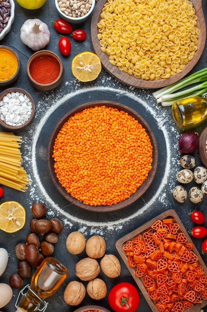 Vista dall'alto lenticchie arancioni crude con uova noci verdure pasta cruda e condimenti su sfondo scuro foto a colori della cucina della torta di dieta del pasto crudo