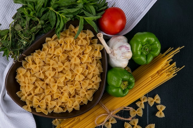 黒い表面に白いタオルの上にスパゲッティトマトニンニクとミントとピーマンのボウルに生パスタのトップビュー