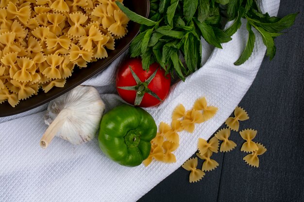 Foto gratuita vista dall'alto di pasta cruda in una ciotola con pomodori aglio e peperoni con menta su un asciugamano bianco su una superficie nera