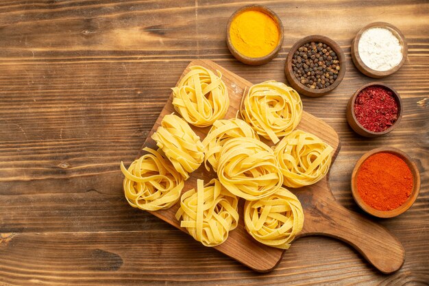 Top view raw pasta designed pasta with different seasonings on brown wooden background dough meal food pasta