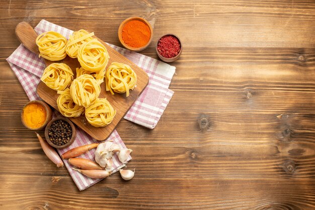 Top view raw pasta designed pasta with seasonings on brown wooden background dough meal food pasta