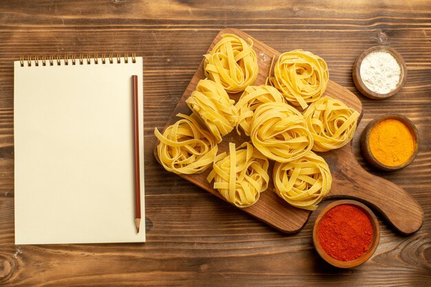 茶色の背景にさまざまな調味料を使った生パスタ生地の上面図生地ミールフードパスタ