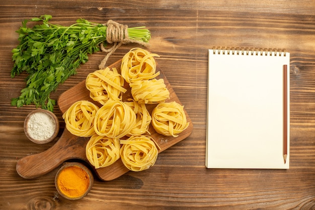 Vista dall'alto impasto di pasta cruda con condimenti e verdure sulla pasta alimentare farina di sfondo marrone