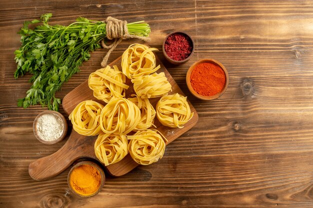 Top view raw pasta dough with seasonings and greens on a brown background dough meal pasta food raw