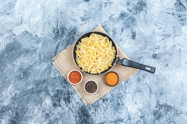 Top view raw pasta in pan with spices on plaster and piece of sack background. horizontal