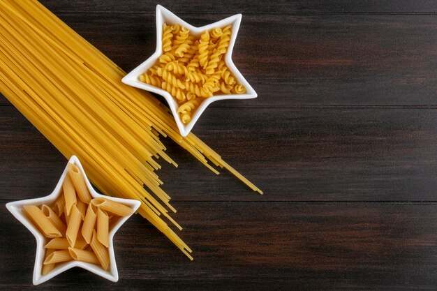 Top view of raw pasta in star shaped saucers with raw spaghetti on a wooden surface