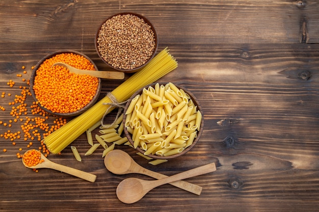 Free photo top view raw pasta with buckwheat and lentils on brown surface