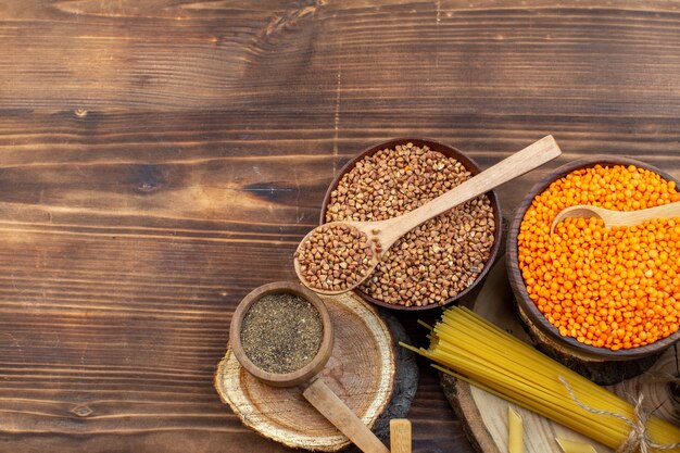 Top view raw pasta with buckwheat and lentils on brown surface