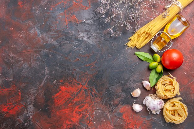 Top view raw pasta with oil and tomatoes on a dark surface dough raw pasta